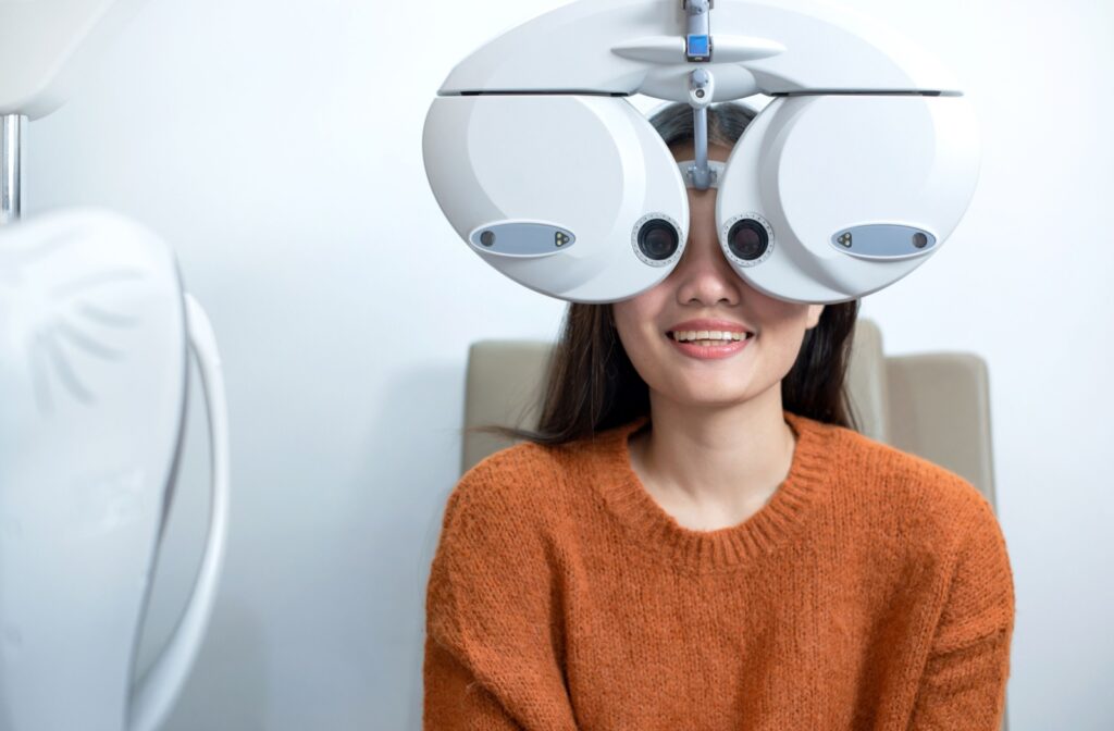 A patient smiling in the exam chair while sitting behind the phoropter.