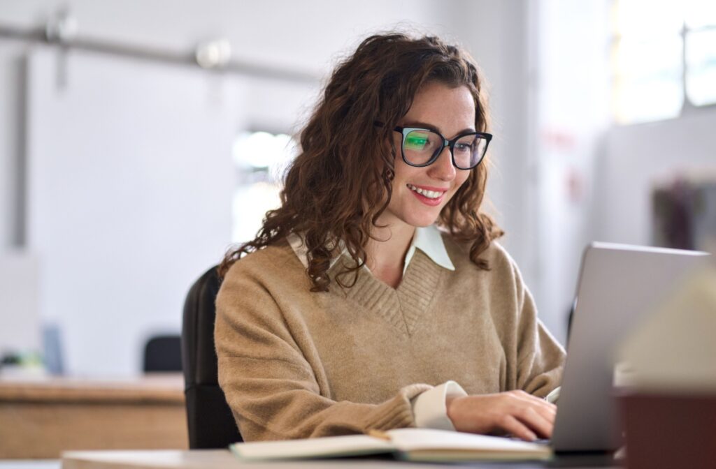 A woman working on a computer, smiling and comfortably wearing Neurolenses.