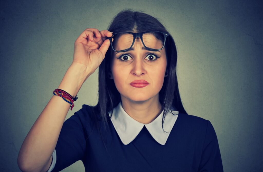 A concerned young adult lifts their glasses from their eyes, showing worry about glasses impacting their vision