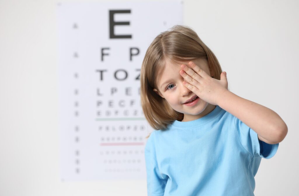 Young girl covering one eye during a vision test with an eye chart in the background.