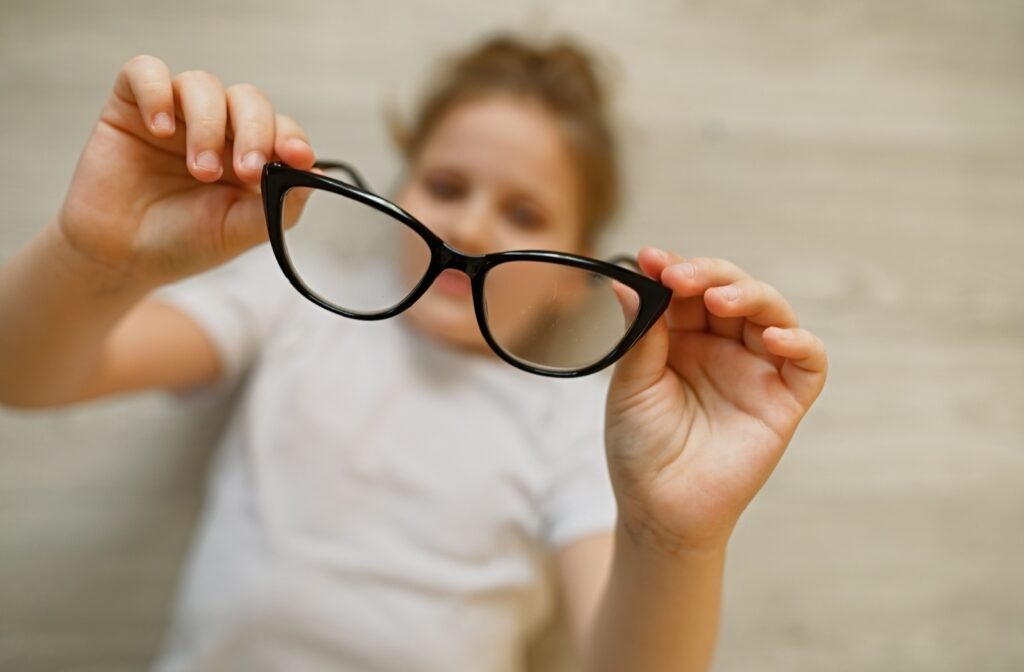 Child holding eyeglasses used for myopia control with MiYOSMART lenses.