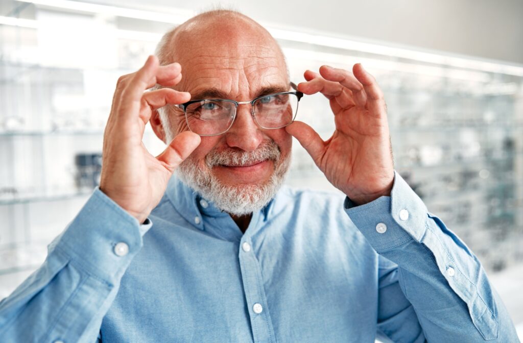 A senior person holds the pair of thin metal glasses they are wearing on their face while standing in an optometry clinic.