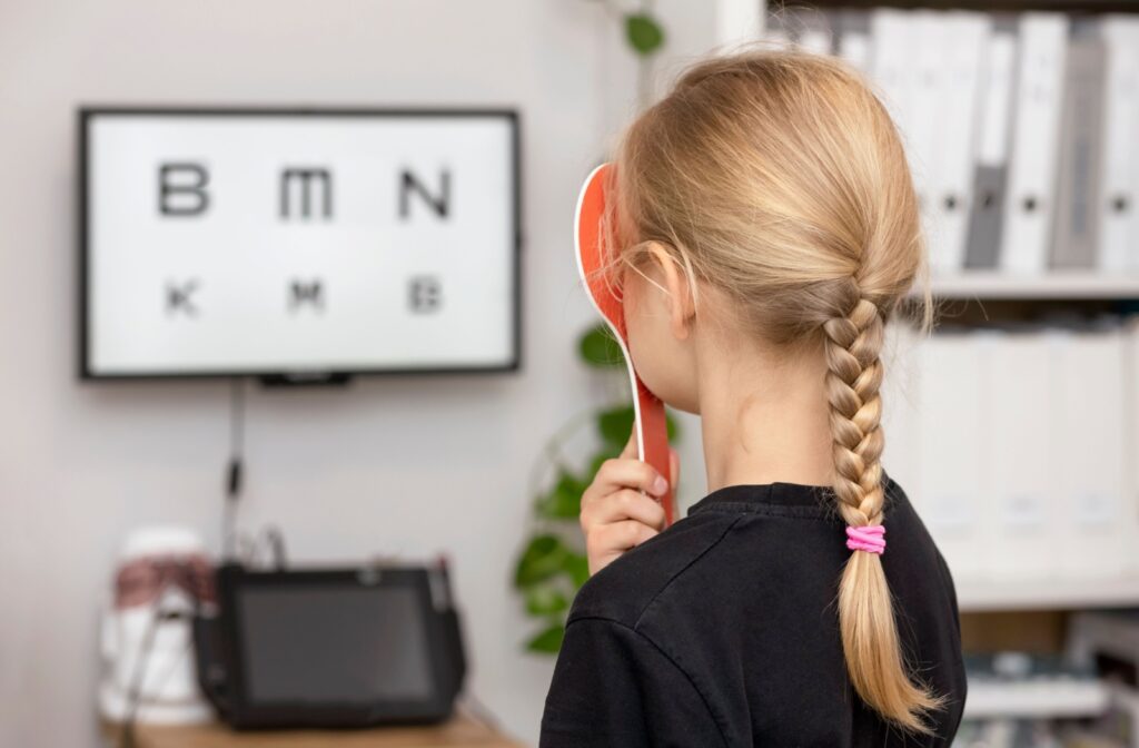A young child covers one of their eyes during an eye test for myopia