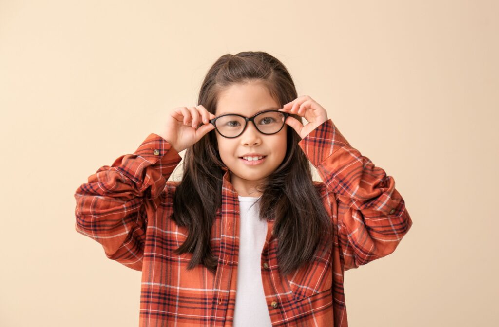 A young child wearing a plaid flannel puts glasses up to their face to help correct their myopia
