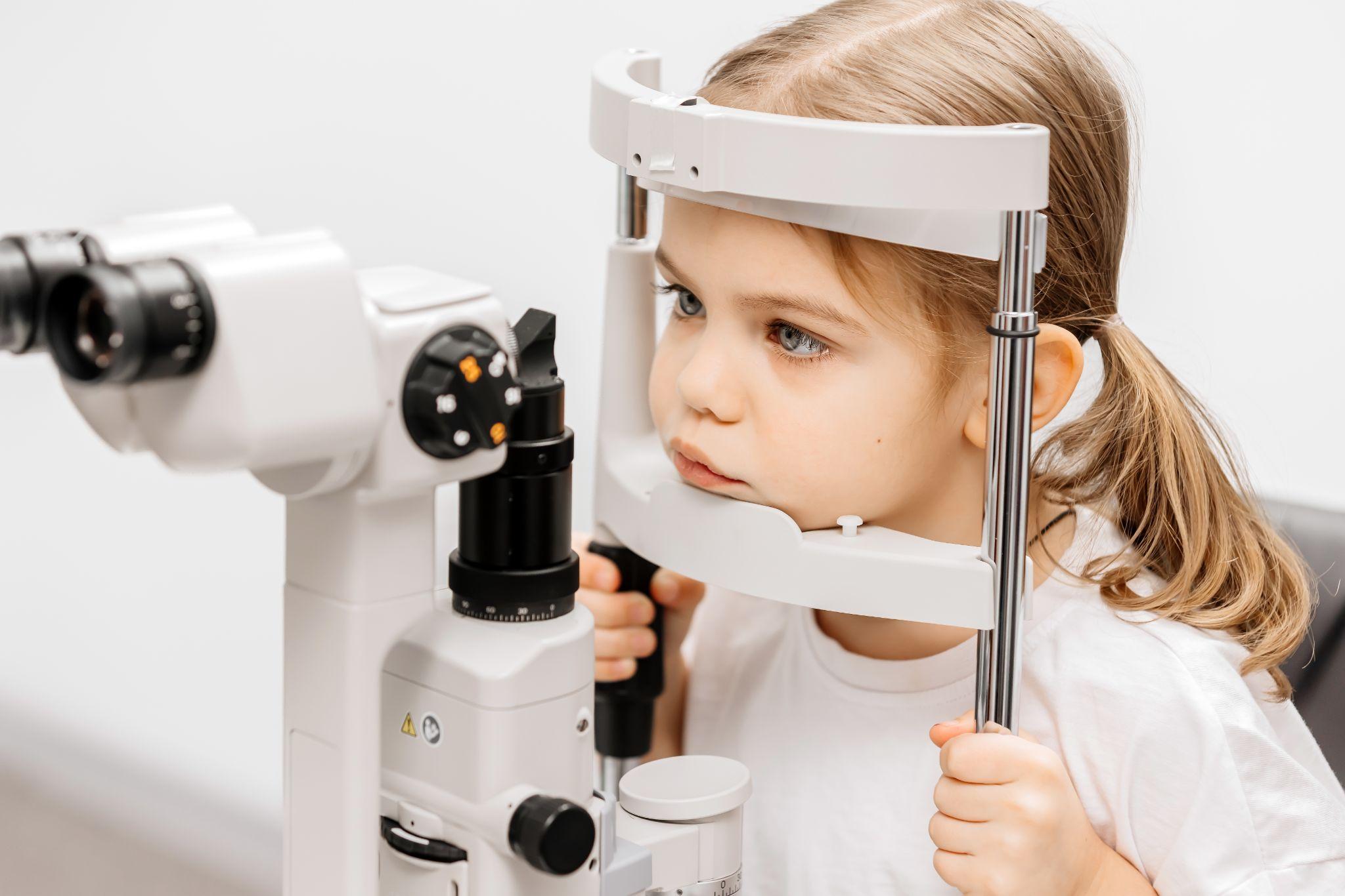 a child resting their chin on a piece of eye exam equipment.