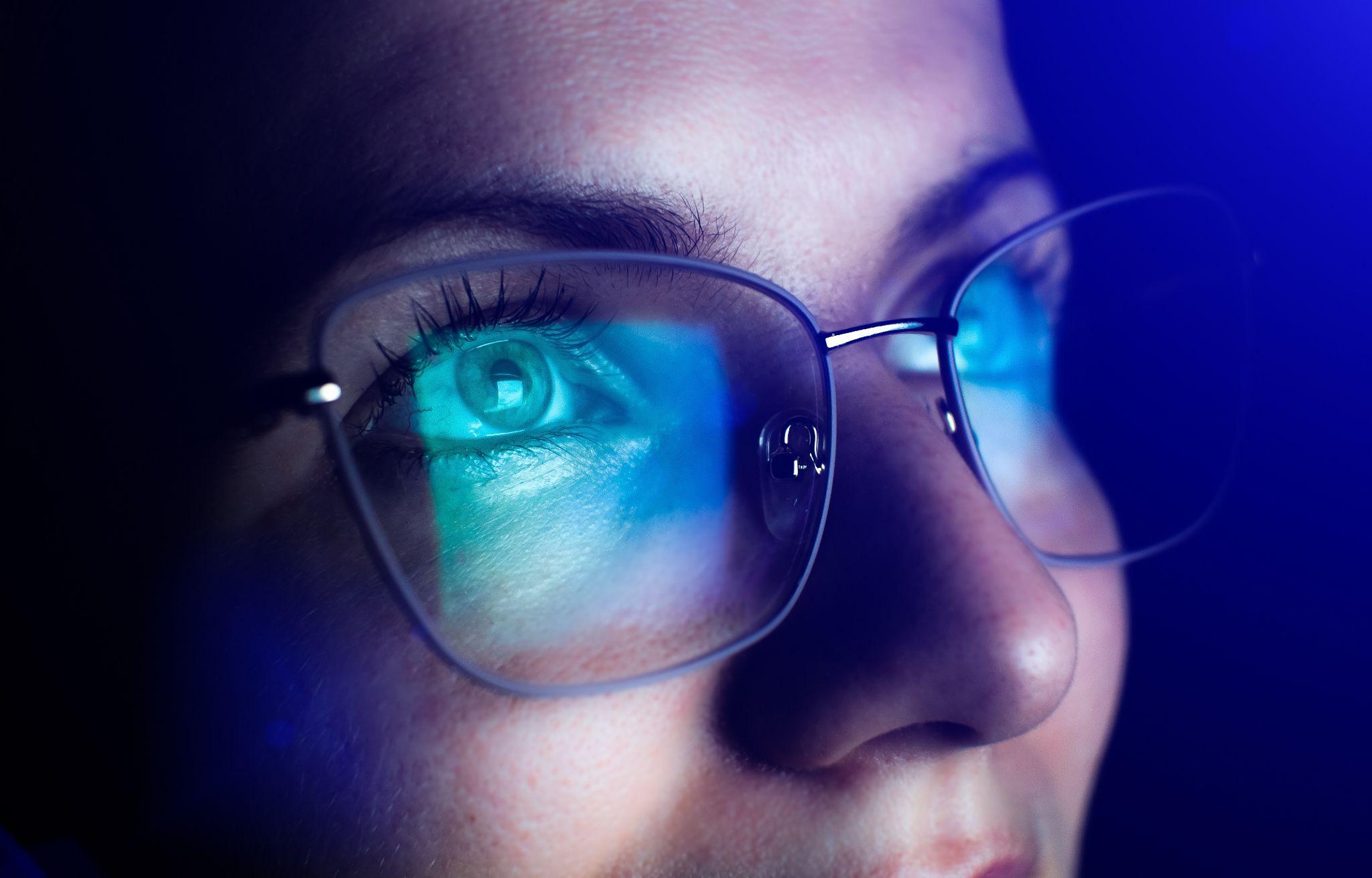 A phone screen being reflected on someones glasses in a dark room